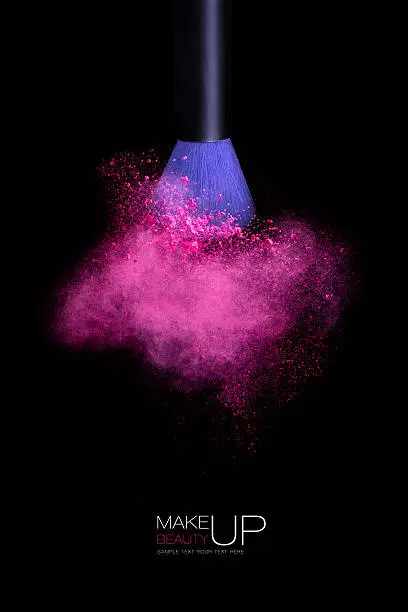 Makeup concept with a single blue makeup brush shaking or applying pink powder. Colorful dust explosion. Isolated on black background with copy space and sample text