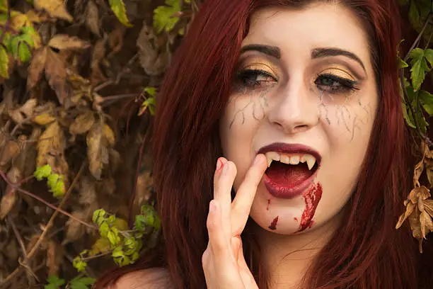 Photo of Redheaded teen vampire outdoors, touching fangs.