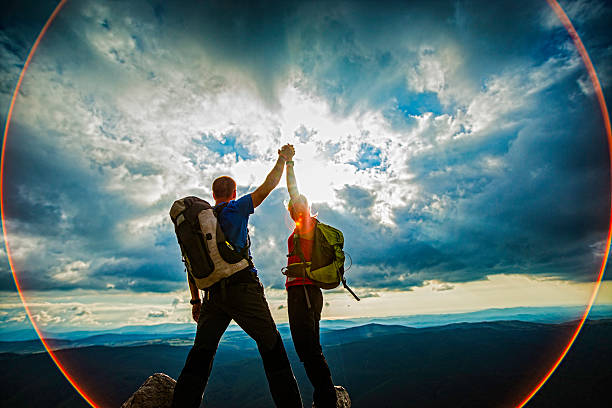 casal no topo de uma montanha aperto de mãos levantadas - mountain climbing rock climbing adventure incentive - fotografias e filmes do acervo