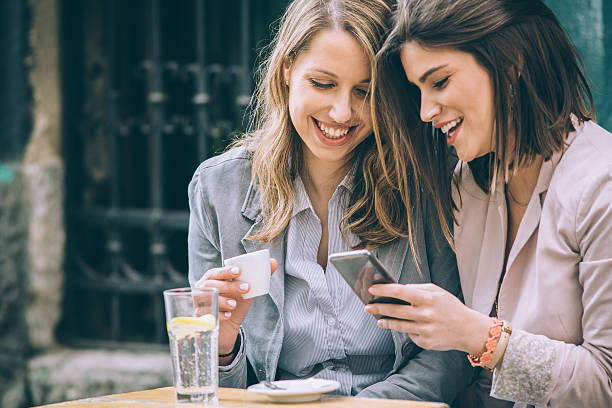 Two woman at cafe Two beautiful young woman sitting at cafe drinking coffee and looking at mobile phone 3686 stock pictures, royalty-free photos & images