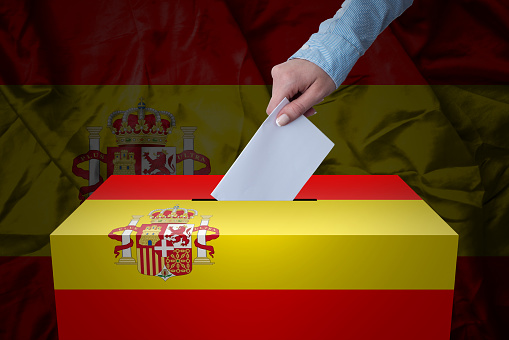 A hand casting a vote in a ballot box for an election in the Spain