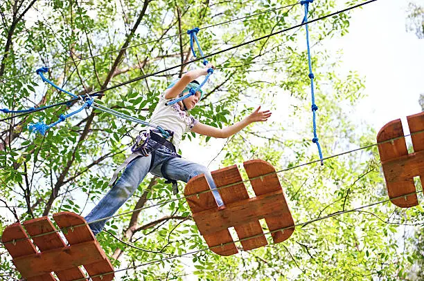 Girl is climbing to high rope structures in forest