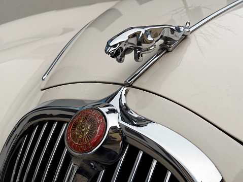 Erlangen, Germany - March 28, 2016: Beige front view of a Jaguar 3.4 litre vintage sports car: detail of car's symbol and hood on a cloudy day.