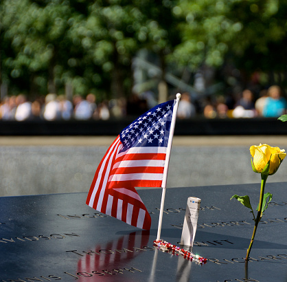 New York City, USA - September 12, 2014: A small American flag, mementos and a yellow rose at the National September 11 Memorial, Ground Zero, World Trade Center, Lower Manhattan.