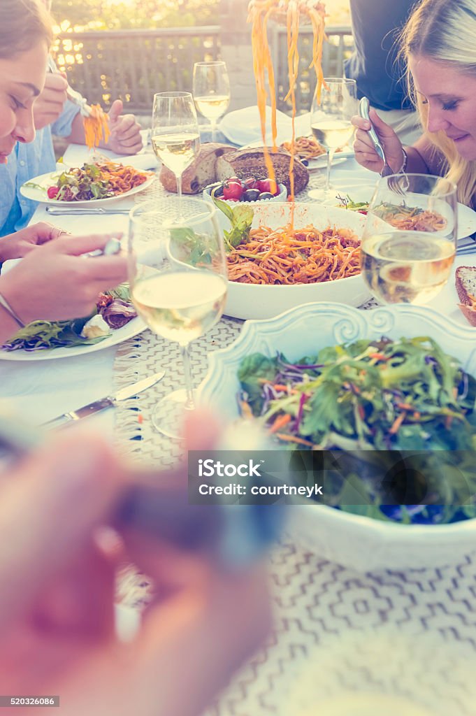 Group of friends having a meal outdoors Group of friends having a meal outdoors. All are hungry and eating. Candid shot.  There are bowls of food on the table including salad and spaghetti Bolognese. There are also glasses of wine.  Multi ethnic group. Friendship Stock Photo