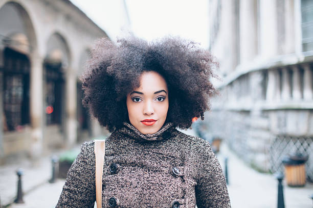 Portrait of curly young woman on street. Front view of head and shoulders. Woman with curly hair  and black coat. Building exterior. Columns as background.