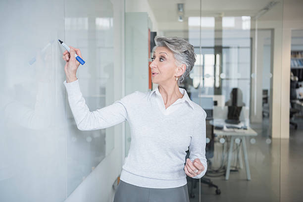 istock Mature woman writing on whiteboard with marker pen 520329164