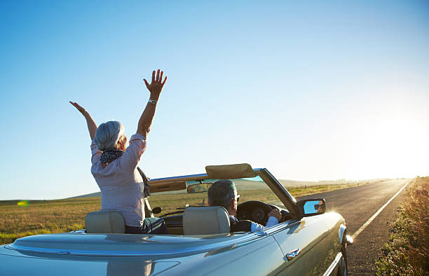 Nothing but the open road Rear view shot of a mature woman raising her hands iin the air while on a roadtrip with her husband convertible stock pictures, royalty-free photos & images