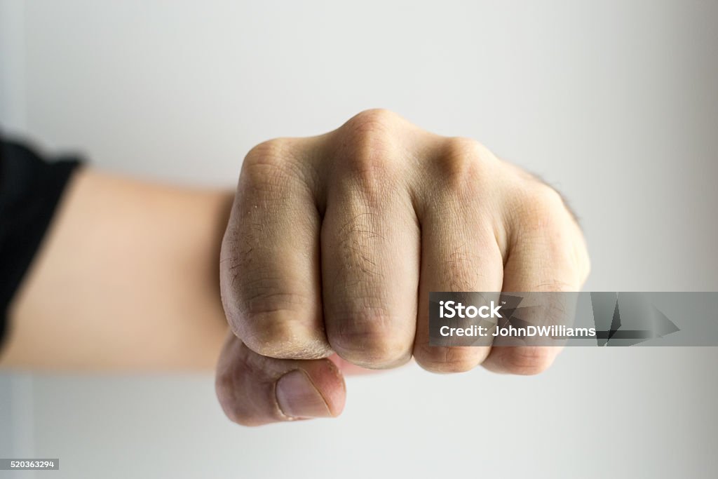 Clenched White Male Fist Boxing Close up image of a white males single clenched fist punching towards the viewer or frame. No rings or markings on the mans hand. Copy space area for crime or fear based concepts and ideas. White backdrop. Fist Stock Photo