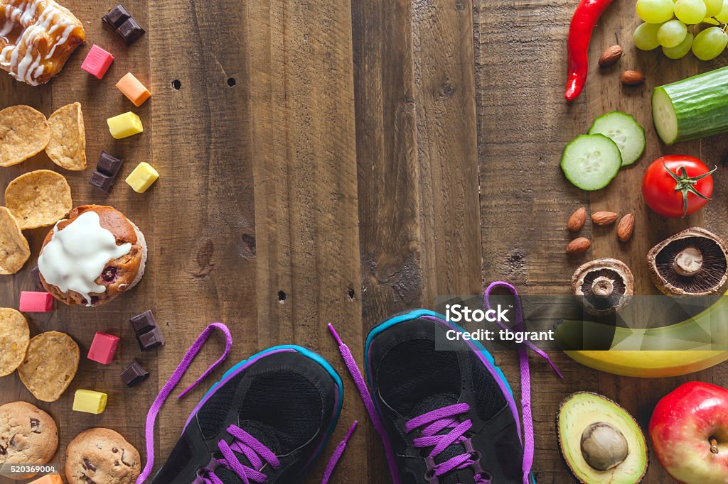 Healthy food, unhealthy food and exercise Running shoes caught between healthy fruit and vegetables and unhealthy cookies, muffin and candy Healthy Eating Stock Photo