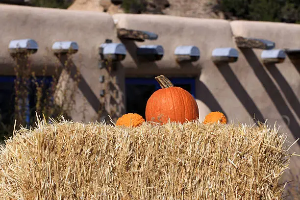 New Mexico autumn scene of gourds atop a haybale, adobe casita in background