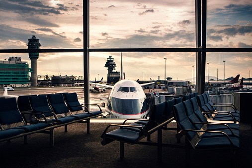 A clean wide angle view of an airline terminal seating area, silhouettes of the chairs against a bright sky and an airplane in the background.  Taken at Hong Kong International Airport (HKG); horizontal image with copy space.