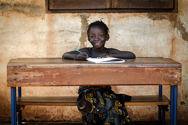 school: orgullosa niña en edad escolar africana sonriente sentado en su escritorio - africa african descent education child fotografías e imágenes de stock