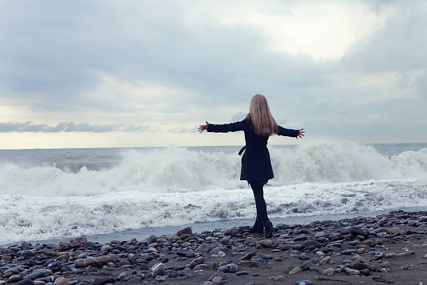 istock Woman in a black coat on the beach 520409720