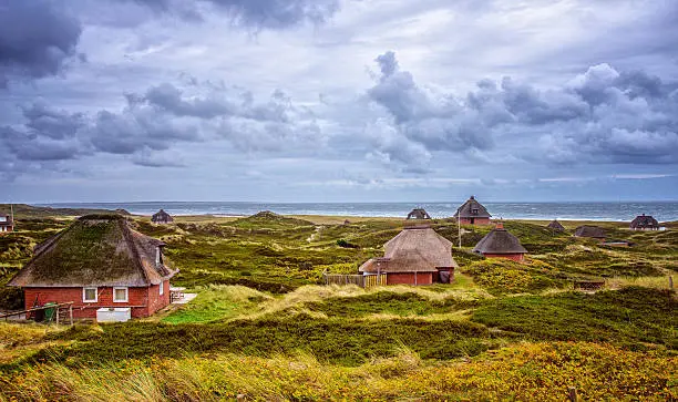 Autumn scenery at Hörnum, Sylt (Germany). Thatched cottages in the dunes under dramatic sky.