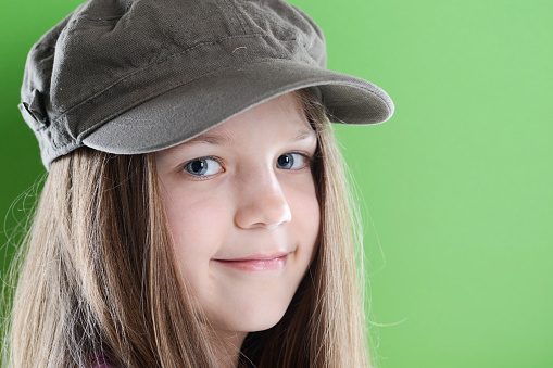 smiling girl in peaked cap with long hairs over green background