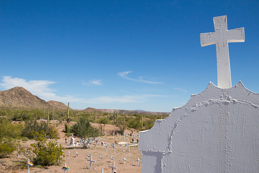 A view of a cross atop a tombstone in a remote cemetery in the Arizona desert.