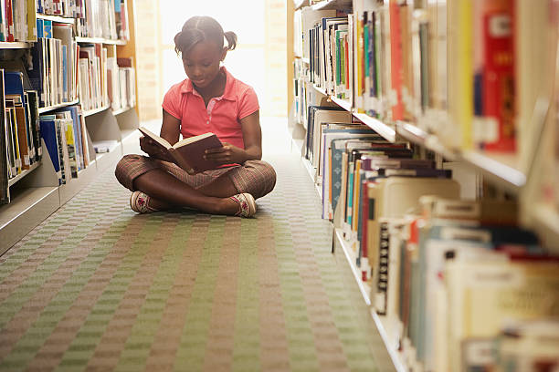 Girl reading at the library Girl reading at the library kid sitting cross legged stock pictures, royalty-free photos & images