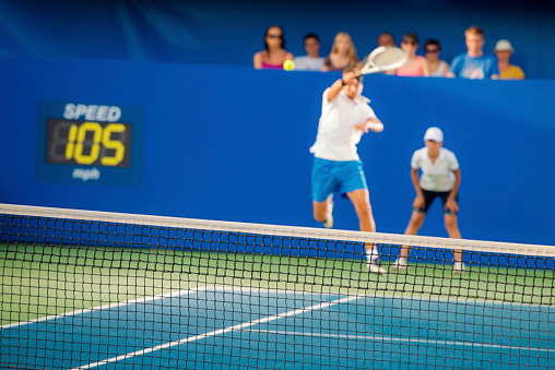 Male tennis player hitting the ball, spectators and line judge in the background., focus on net.