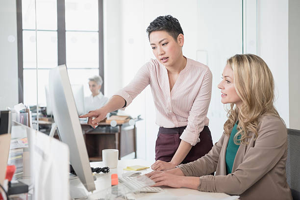 Mid adult woman using computer, young woman pointing
