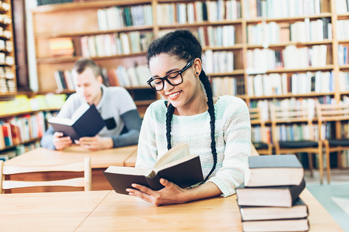 Schoolgirl searching and choosing books from a bookshelf in the library. Education, literature, and new edition concepts.