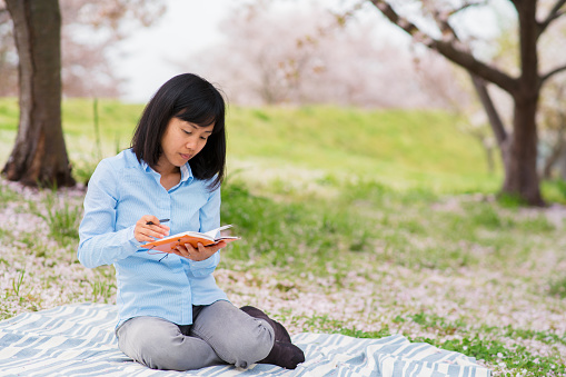 Woman writing in a diary outdoors in the park. Okayama, Japan. April 2016