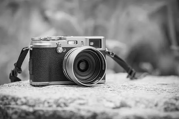 Vintage-style digital camera on boulder over blurred nature background. Shallow depth of field with focus on camera. Outdoor. Black and white picture style.
