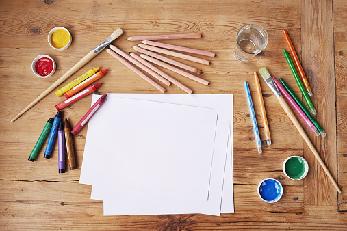 Blank paper with painting supplies and pencils on a wooden table