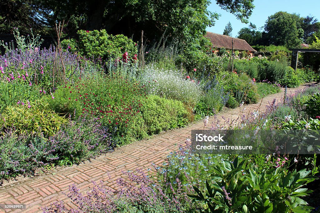 Image of red-brick path through herbaceous flower border, cottage garden Photo showing an old block paved pathway, with weathered / aged red bricks that are full of character.  The bricks in this path have been laid out in a traditional alternating 'basketweave' pattern, while some are simply in lines, sideways and lengthways on ('stacked bond' style), defining the edges and pattern.  This simple footpath leads through a garden of herbaceous flowers, which can be seen growing of the edges of the path and softening its appearance. Asphalt Stock Photo