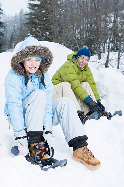 junges paar bindet schneeschuhe in waldnähe, porträt - snowshoeing snowshoe women shoe stock-fotos und bilder