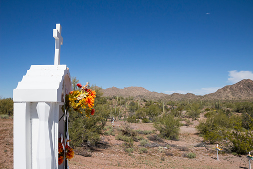 A tombstone with a cross and flowers in a cemetery in a remote part of the Arizona desert.