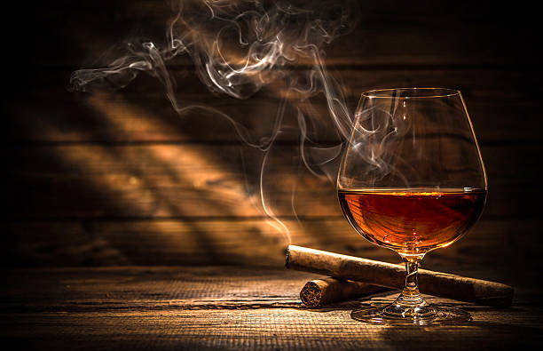 Whiskey with smoking cigar Glass of whiskey with smoking cigar and ice cubes on wooden table cigar photos stock pictures, royalty-free photos & images