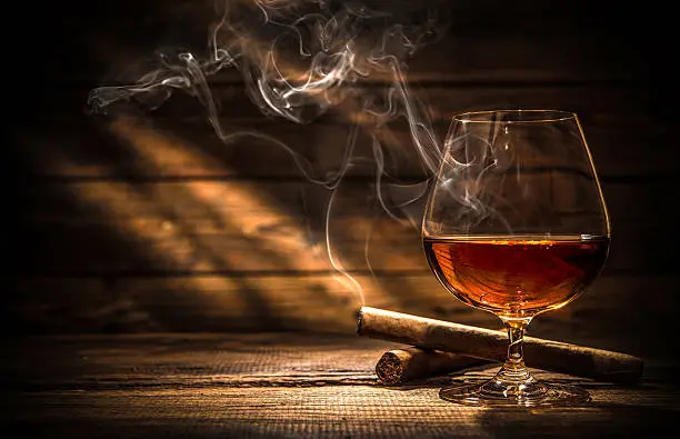 Glass of whiskey with smoking cigar and ice cubes on wooden table