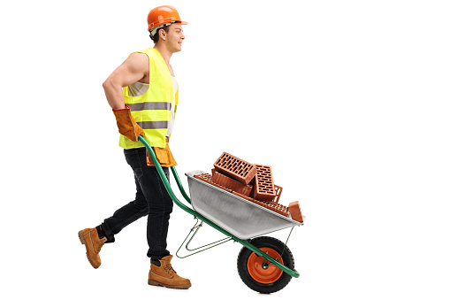 Construction worker pushing a wheelbarrow full of bricks isolated on white background