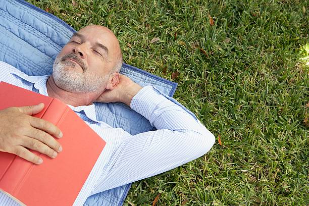 uomo che sonnecchia con un libro sul petto - men reading outdoors book foto e immagini stock