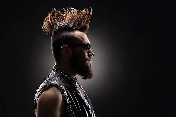 Profile shot of a young punk rocker with a Mohawk hairstyle on dark background
