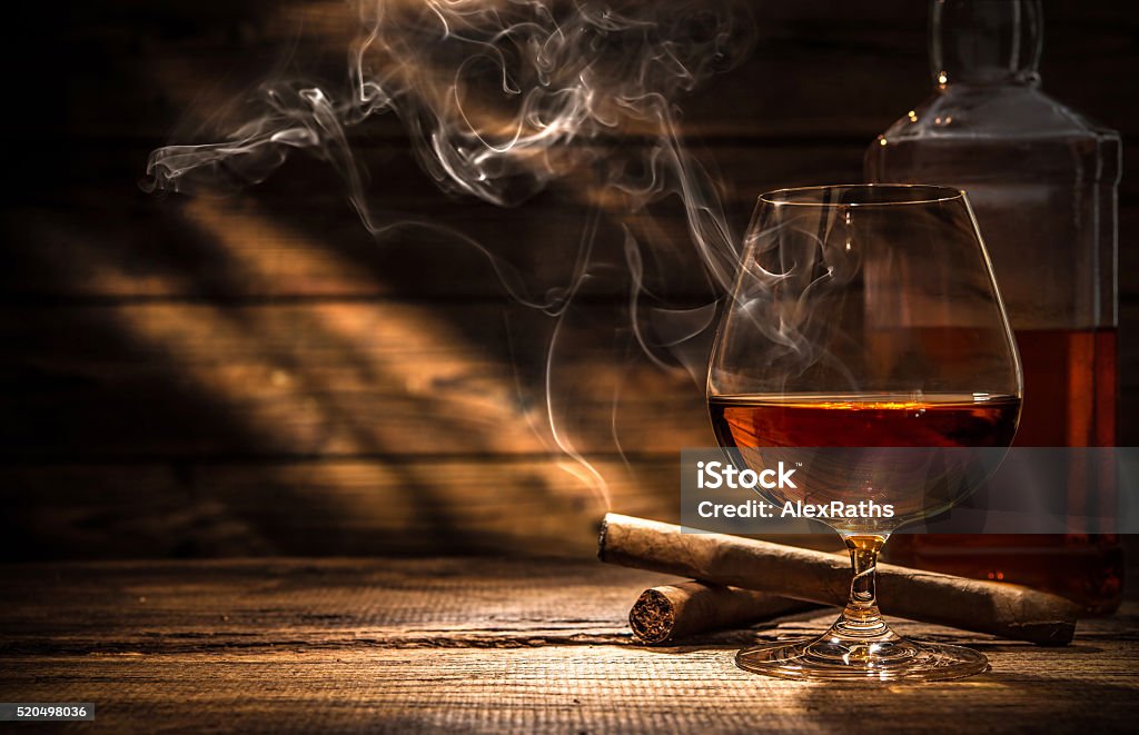 Whiskey with smoking cigar Glass of whiskey with smoking cigar and ice cubes on wooden table Cigar Stock Photo