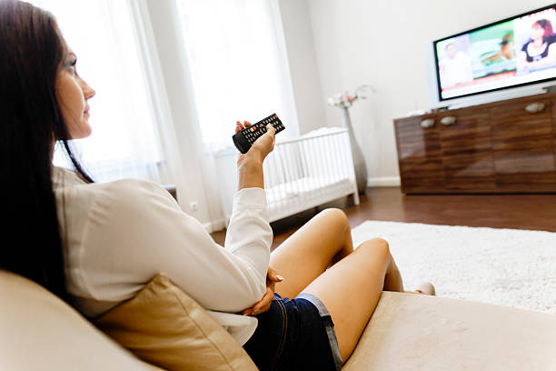 istock Beautiful young woman using remote control in living room 520498580