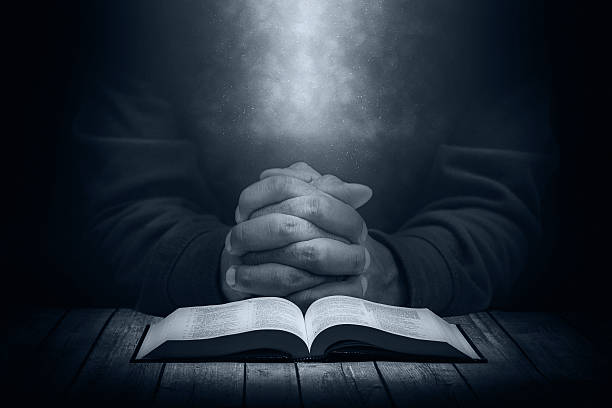 istock Man praying on a wooden table with an open Bible 520498584