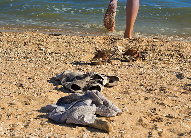 Horizontal landscape of a woman's bare feet walking along the wet sand at Byron Bay, popular travel destination on the north coast of NSW. Part of her dress is visible.