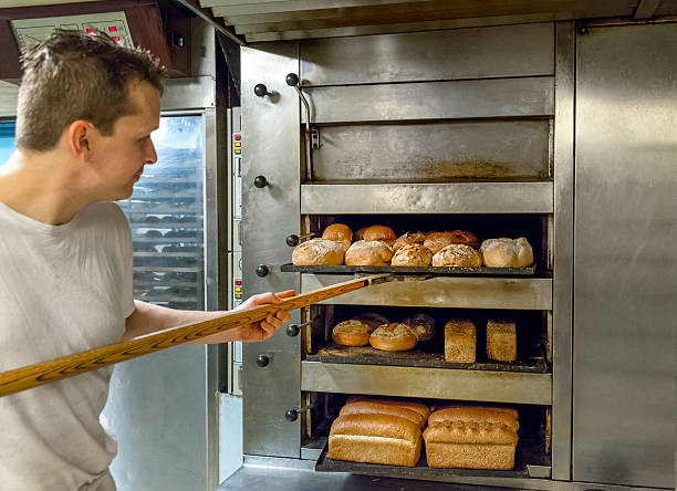 Baker taking bread out of oven Fresh artisan bread taken out of the oven. baker occupation stock pictures, royalty-free photos & images