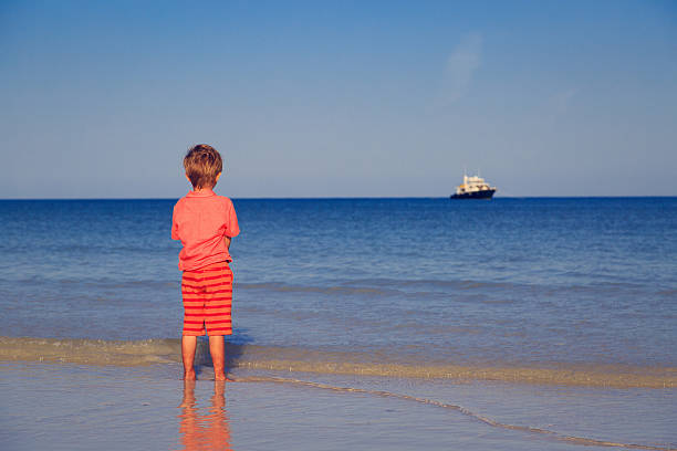 Little boy looking on big ship at sea, travel concept