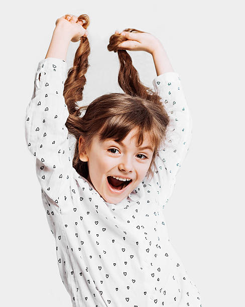 Cute little girl holding her hair Pretty little girl gives a toothy smile. Isolated on gray background Pigtails stock pictures, royalty-free photos & images