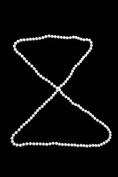 Thread of faux pearls in the shape of hourglass on black background