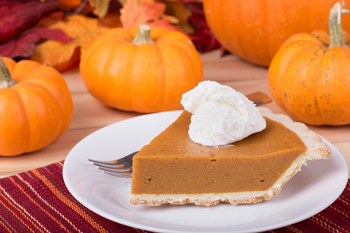 Slice of pumpkin pie with whipped topping and pumpkins in background