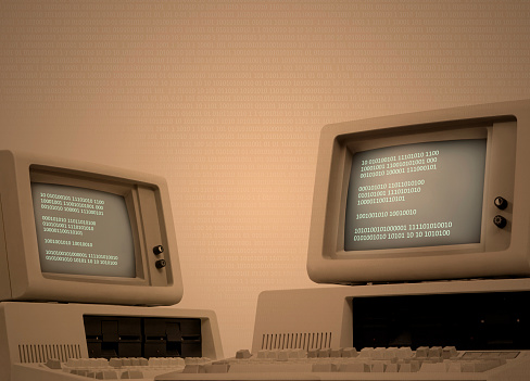 Vintage technology beige background with two old computers showing binary code on its monitor. Code spreads across image area. Retro revival of seventies devices. Plenty of copy space on the side. Low-key background for easy costumization. 