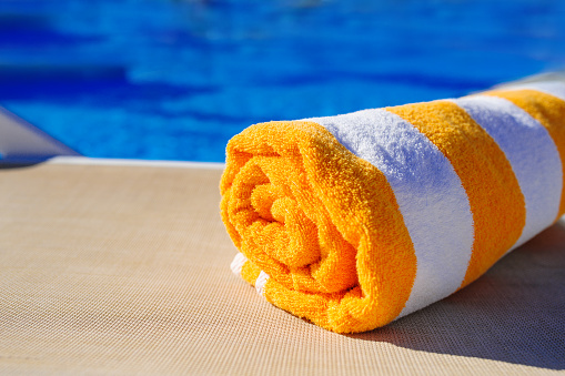 orange with white towel on a sun lounger on background of pool.