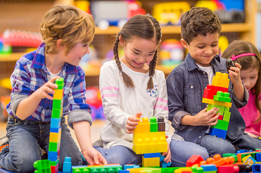 A multi-ethnic group of elementary age children are playing with plastic blocks in class.