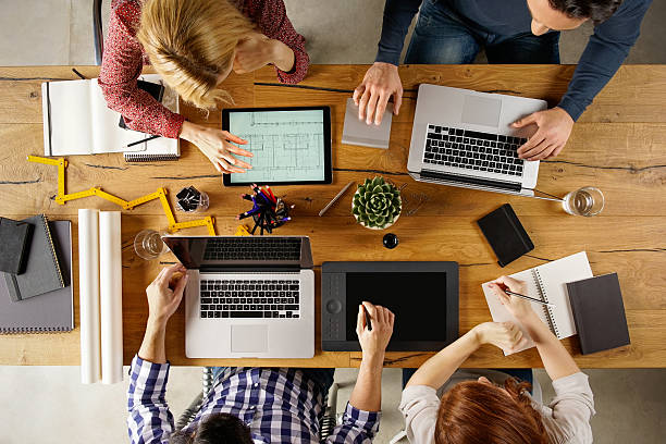 Architects at work Top view of team working on blueprint. High angle view of architects working on a construction project. Young group of people sitting in office and working together on a new project. small office stock pictures, royalty-free photos & images