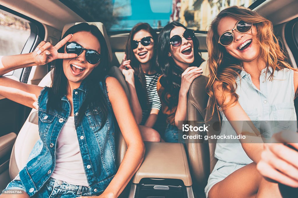 Just fun and road ahead. Four beautiful young cheerful women looking happy and playful while sitting in car Car Stock Photo
